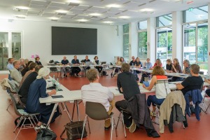 Viele Menschen sitzen an Tischen an Stühlen und sprechen angeregt miteinander in einem hellen Raum. - Foto: Detlef Podehl