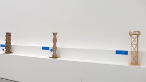 Drei Modelle zum Thema Turmbau aus Holz stehen auf Sockeln vor einer weißen Wand.