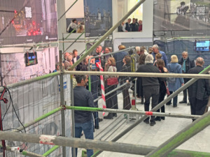 Personen stehen in einem hellen Raum, in dem Bauzäune mit Transparenten hängen.