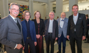 Sechs Personen stehen vor einer Menschengruppen und lächeln in die Kamera.