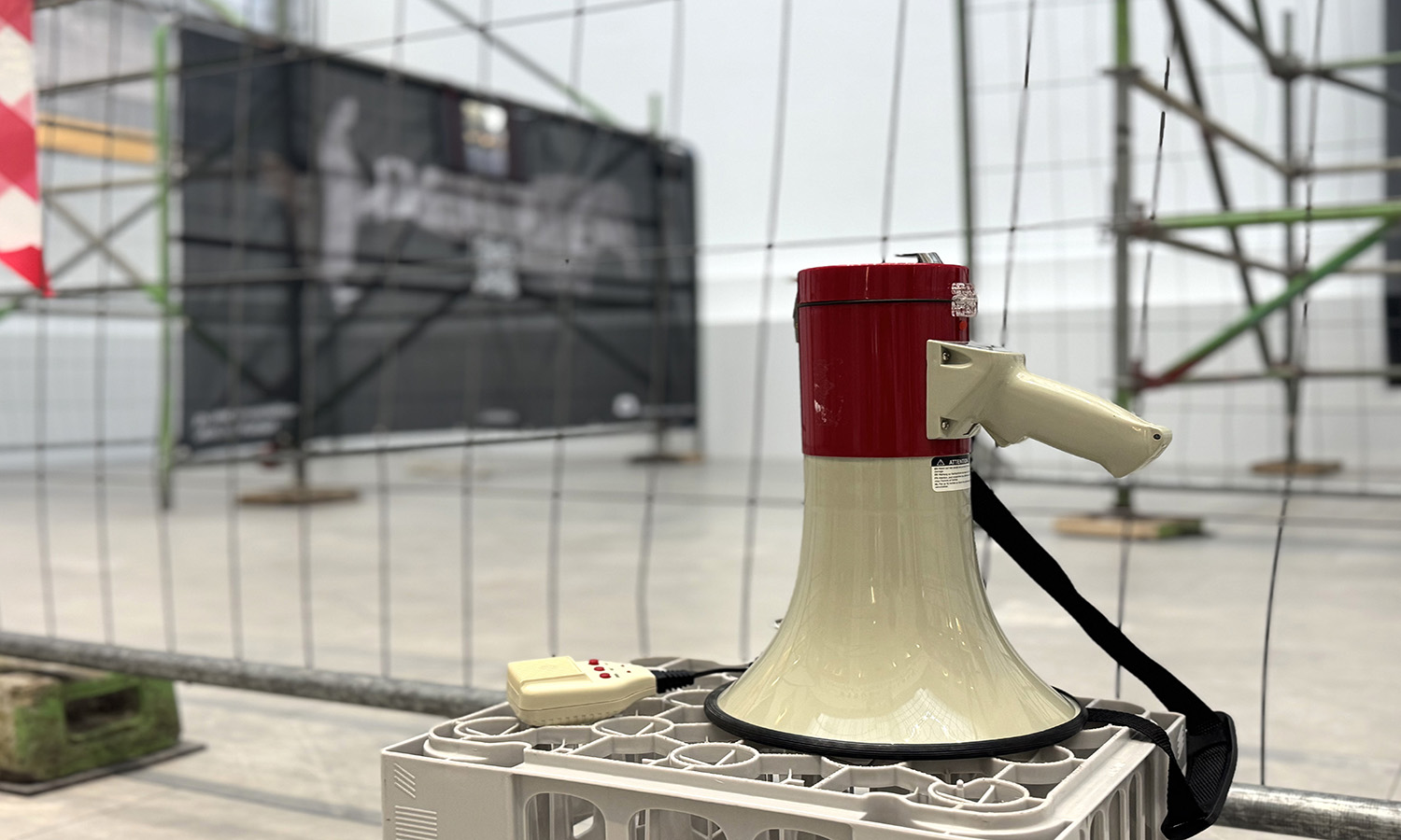 Eine Megafon liegt auf einer Kiste, dahinter sind Bauzäune, teilweise bespannt mit Plakaten.