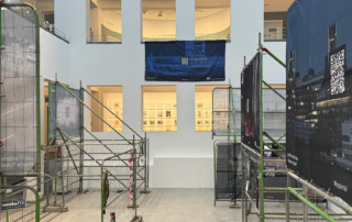 Bauzäune mit Bannern und Plakaten stehen in einem hellen Raum.