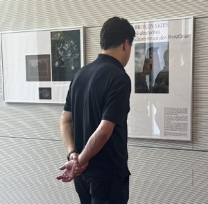 Eine Person steht vor einer Dokumententafel und betrachtet abgebildete Texte und Bilder.