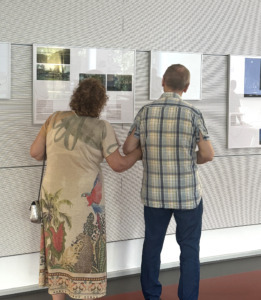Zwei Personen stehen vor Foto- und Texttafeln und schauen sich eine Ausstellung an.